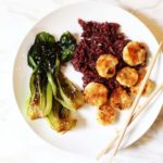 White plate of Baked Sweet and Spicy Coconut Shrimp with Seared Bok Choy and Purple Rice with chopsticks on the plate