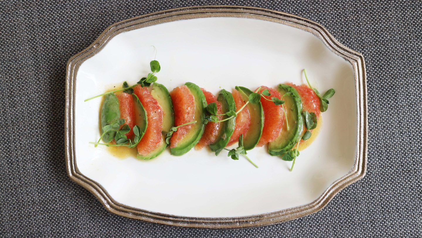 Pink Grapefruit and Avocado Salad on a white plate drizzled with vinaigrette and garnished with microgreens 