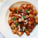 White bowl of Cauliflower Gnocchi with tomato sauce and topped shaved parmesan and fresh basil