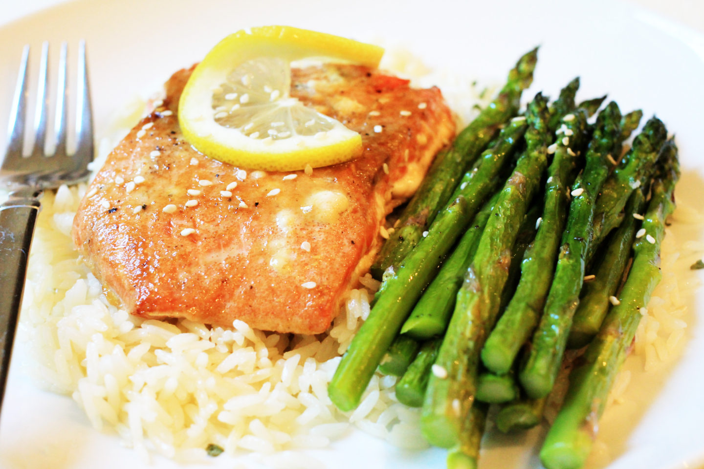 close up of salmon with lemon slice on rice rice and asparagus