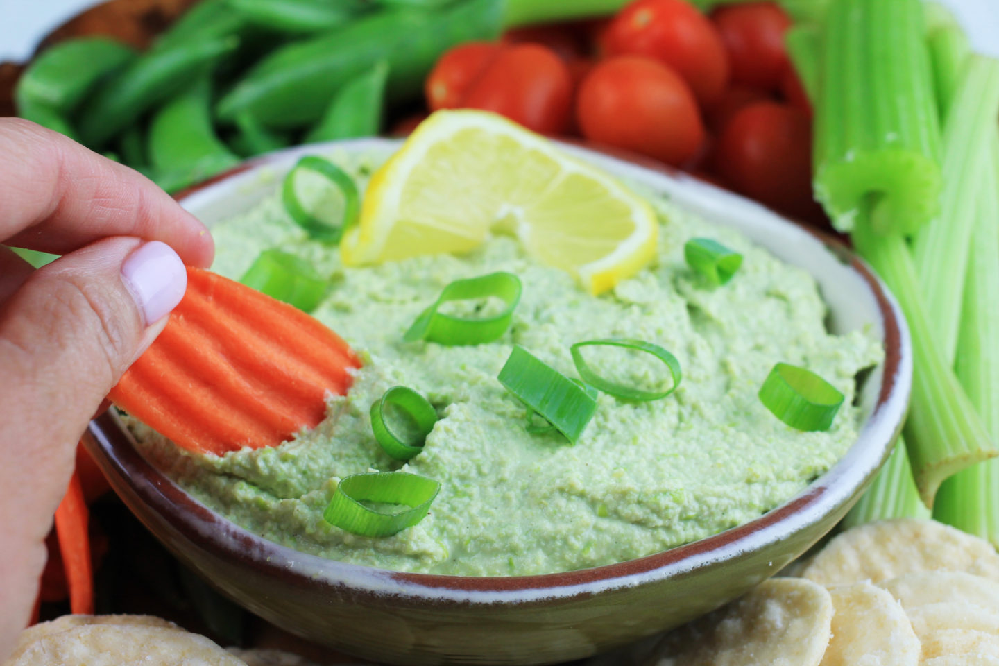 Hand dipping into Edamame Hummus with Carrot