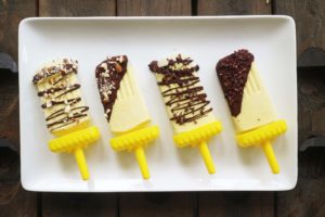 Four Vegan Orange Creamsicle Ice Popsicles coated in chocolate on a white tray