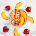 Peach and Strawberry Smoothie Bowl in a white bowl with sliced peaches and fresh strawberries surrounding the bowl