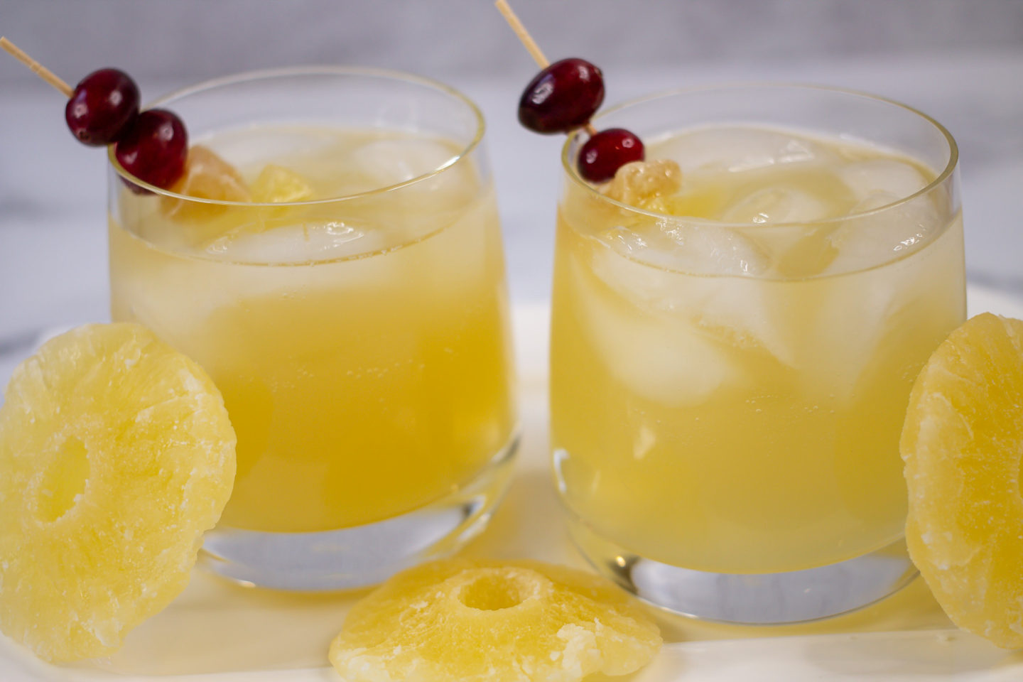Two Glasses of Mexican Mule Cocktails with Fresh Cranberries and Dried Ginger and Pineapple garnish with rounds of dried pineapple