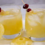 Two Glasses of Mexican Mule Cocktails with Fresh Cranberries and Dried Ginger and Pineapple garnish with rounds of dried pineapple