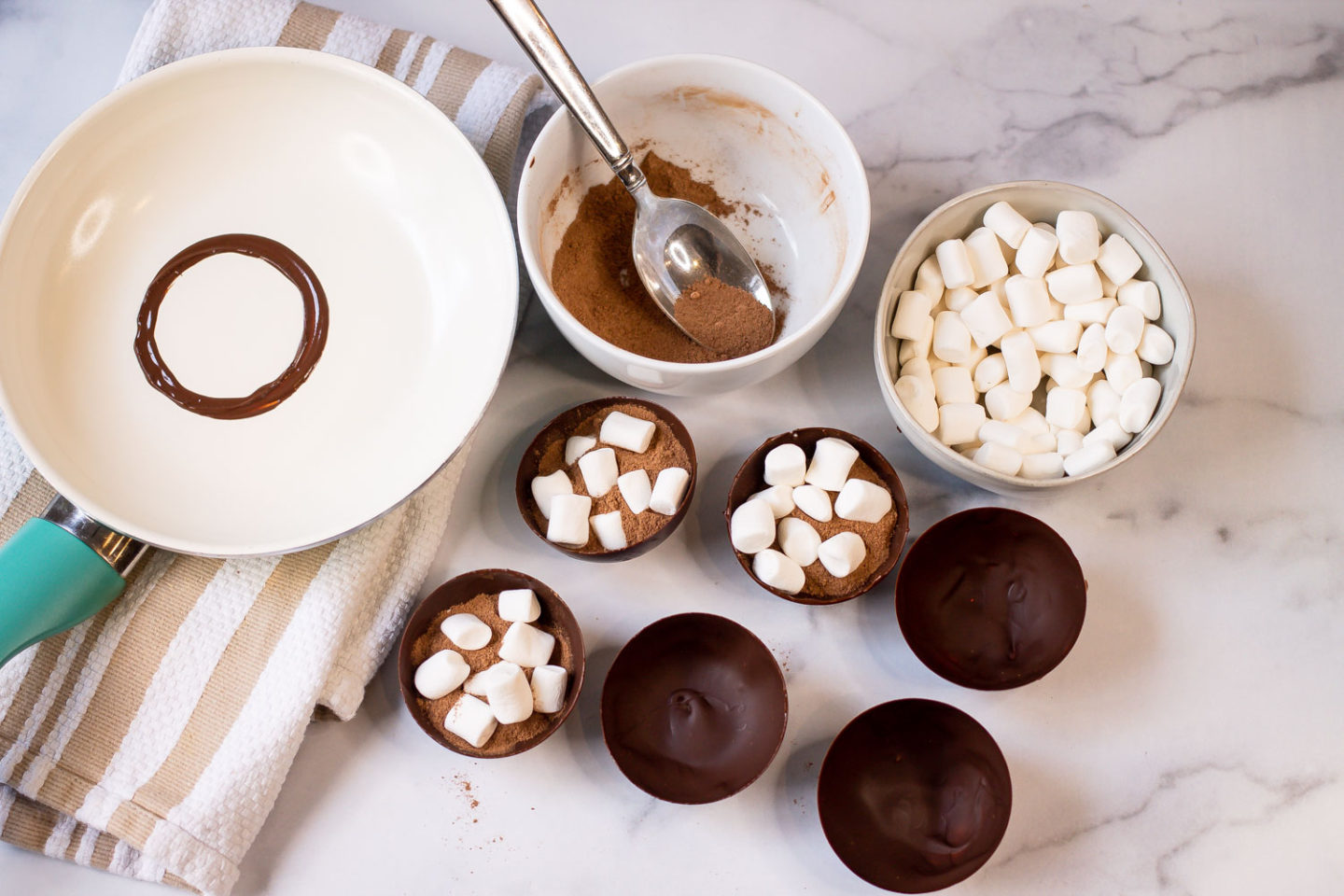 Chocolate Mold Halves filled with hot cocoa mix and mini marshmallows with a hot skillet and a bowl of hot cocoa mix