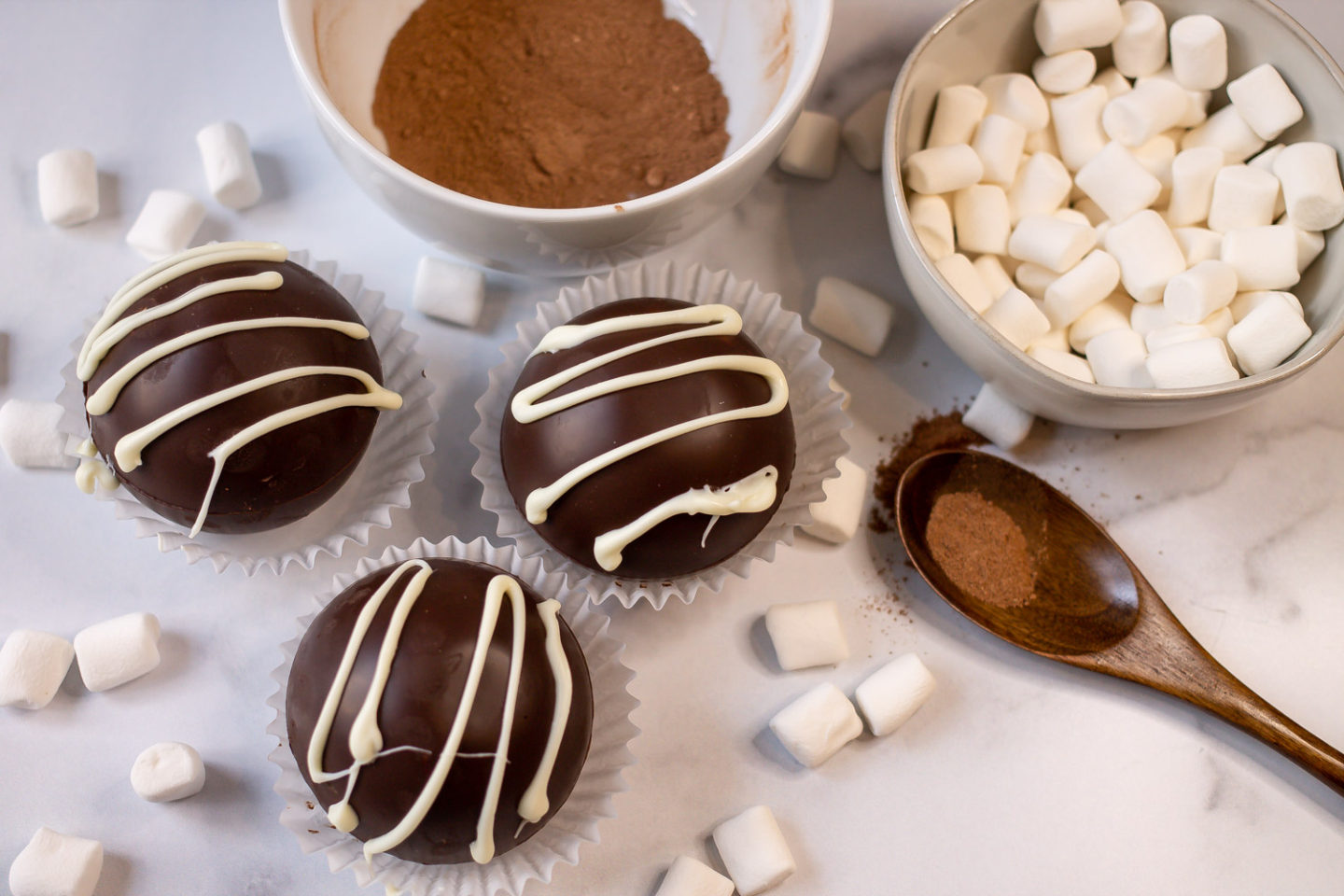 3 Hot Cocoa Bombs with a bowl of mini marshmallows and a bowl of hot cocoa mix