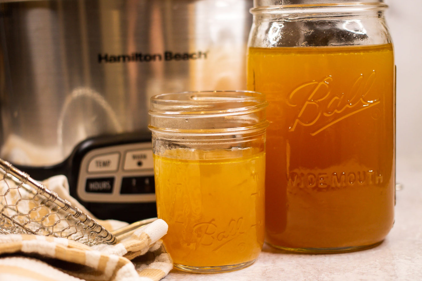 Two jars of homemade chicken bone broth with a slow cooker in the background