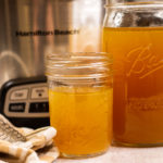 Two jars of homemade chicken bone broth with a slow cooker in the background