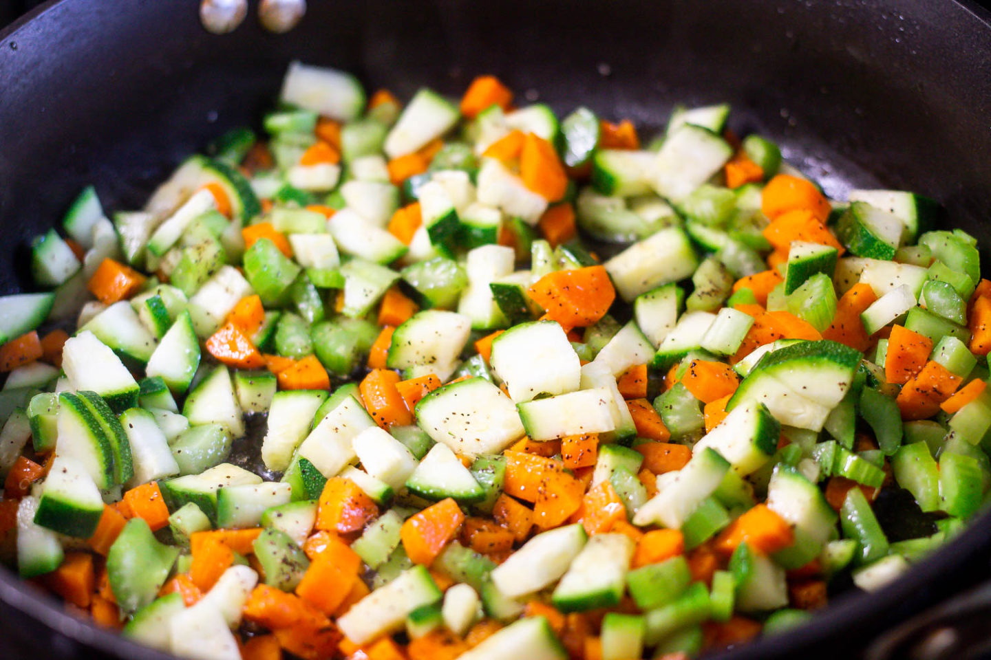 A saute pan filled with diced carrots, celery, zucchini